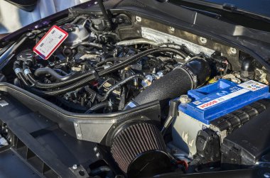 Bir araba motorunun ayrıntılı yakın çekim görüntüsü motor bloğu, çeşitli borular ve hortumlar, pil, silindir filtresi ve şasenin bazı bölümleri içerir.