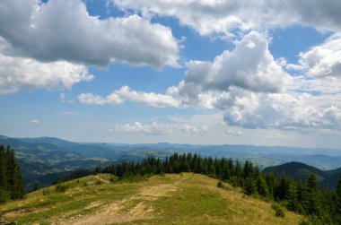 Yoğun ormanlar, yeşil vadiler ve tepelerle kaplı dağların manzaralı yaz manzarası bulutlu bir gökyüzünün altında güneş ışığıyla yıkandı. Karpat Dağları, Ukrayna