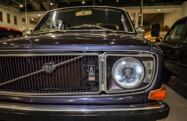 Yakın plan ön far, klasik tasarım ve retro özelliklerini vurgulayan, bir sergi salonunda ikonik bir Volvo 142 araba.