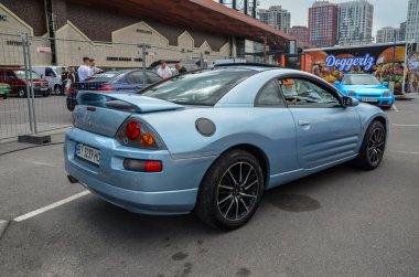 Güçlü motoruyla bilinen parlak mavi spor araba Mitsubishi Eclipse, açık hava otomotiv etkinliğinde uygun fiyata satılıyor.