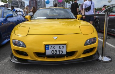 Çarpıcı sarı 1997 Mazda RX-7 FD, klasik bir Japon spor otomobili döner motoru ve ikonik farları ile tanınır.