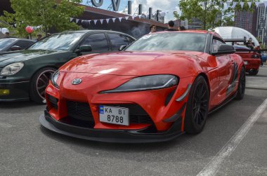 Parlak kırmızı Toyota Supra, modern bir spor araba, açık havada park edilir. Arabanın tamponu ve siyah aksanı modifiye edilmiş.