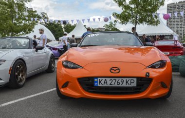 Turuncu spor araba Mazda MX-5 popüler iki koltuklu üstü açık arabasının kendine has geri çekilebilir üstü açık çatısı vardır.