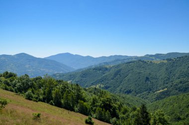 Berrak mavi gökyüzünün altında yuvarlanan yeşil tepeleri gösteren sakin dağ manzarası, doğanın huzur ve güzelliğinin özünü yakalıyor. Açık hava macerası ya da barışçıl geri çekilme teması için idealdir.