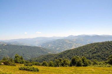 Berrak mavi gökyüzünün altında yuvarlanan yeşil tepeleri gösteren sakin dağ manzarası, doğanın huzur ve güzelliğinin özünü yakalıyor. Açık hava macerası ya da barışçıl geri çekilme teması için idealdir.