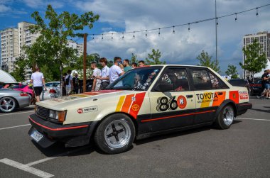 Lassic 1986 Toyota Carina A60, bir açık hava araba fuarında sunulan kutu tasarımı ve güvenilirliğiyle bilinen yarış çıkartmaları.