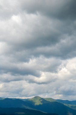 Dramatik bulutlu gökyüzünün altında bir sıradağ manzarası. Gölgeler ve ışık arasındaki zıtlık doğal güzelliği arttırır ve atmosferik bir hava yaratır.