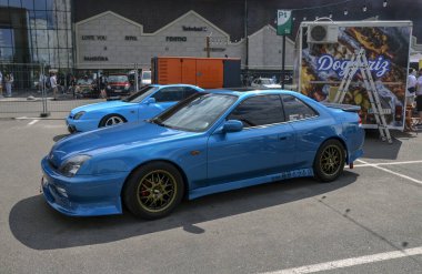 Pırıltılı mavi 1997 Honda Prelude, 1990 'lardan kalma popüler bir Japon spor coupe açık hava etkinliğinde park etmiş, canlı rengi ve modern tasarımı ile dikkat çekiyor.