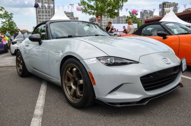 Mazda MX-5 Miata, parlak beyaz dış ve bronz alaşımlı tekerlekleriyle, sürüş zevki ve tasarım zarafetinin bir simgesidir.