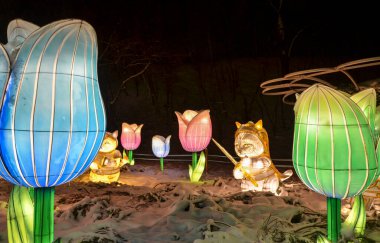 Gece vakti, etrafı karla çevrili parlak lale ışıklarıyla aydınlatılmış kedi figürlerinin yer aldığı sihirli bir atmosfer yaratıyor.