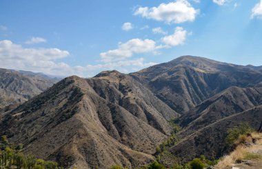 Uçsuz bucaksız dağların ve vadilerin ışıl ışıl beyaz bulutlarla kaplı mavi gökyüzünün altında uzak bir ufuk manzarası. Kafkasya, Ermenistan