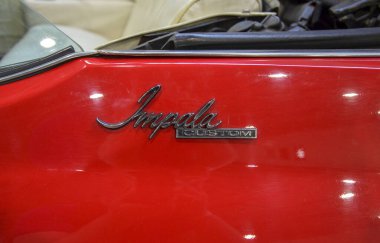 Klasik bir Chevrolet 'ye Impala Özel Rozeti. Parlak krom rozet parlak kırmızı boyaya karşı duruyor, arabanın mirasını ve modelini vurguluyor.