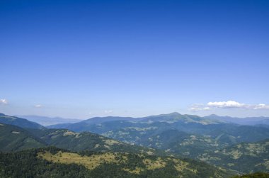 Yuvarlanan yeşil tepeler, yoğun ormancılık ve berrak, geniş mavi gökyüzü içeren dağlık bir manzara. Karpat Dağları, Ukrayna