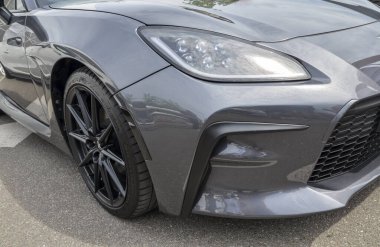 Gri Toyota GR86 'nın ön köşesinde arabanın spor özelliklerini vurgulayan far, siyah ızgara ve ön tampon tasarımı görülüyor.