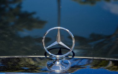 Iconic Mercedes-Benz kaput süsü, üç köşeli bir yıldız krom içinde parıldıyor, parlak bir zemine monte edilmiş, arabanın kaputunun koyu arkaplanına,
