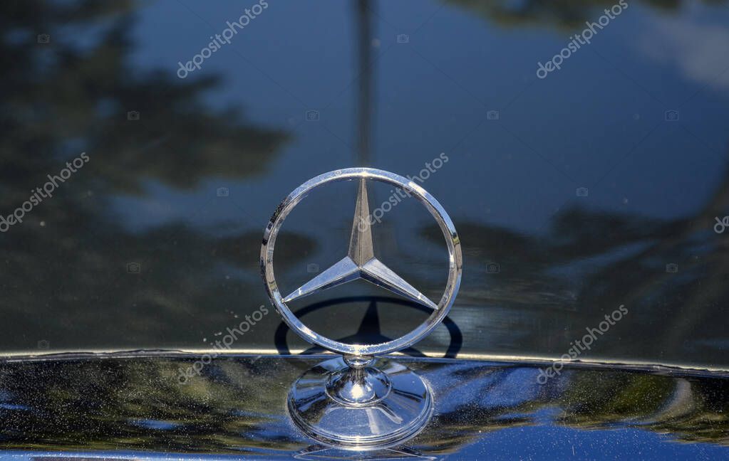 Iconic Mercedes-Benz hood ornament, a three-pointed star gleaming in chrome mounted on a polished base against a dark background, of car's hood