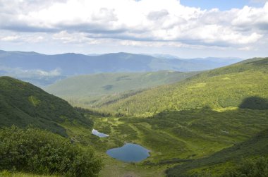 Vorozheska Gölü 'nün bulunduğu güzel dağlık vadi bulutlu bir gökyüzünün altında yemyeşil ormanlarla çevrili, sükuneti ve doğal güzelliği somutlaştırıyor. Svydovets, Karpatlar, Ukrayna