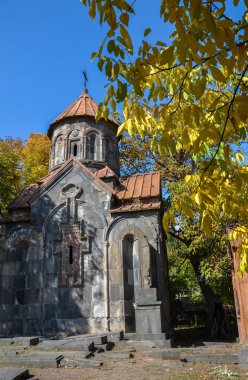 Mashtots Hayrapet Kilisesi, Garni, Ermenistan. Antik taş kilise, açık mavi bir gökyüzünün altında, sonbahar yapraklarıyla ağaçların arasına kurulmuştur. Kilisede kubbeli bir çatı ve karmaşık taş oymalar var.