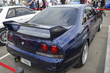 Koyu mavi Nissan Skyline GT-R R33 bir araba etkinliğinde, gösterişli parlak tasarım, ikonik arka spoiler, market tekerlekleri, ve farklı GT-R rozet