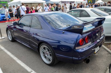 Koyu mavi Nissan Skyline GT-R R33 bir araba etkinliğinde, gösterişli parlak tasarım, ikonik arka spoiler, market tekerlekleri, ve farklı GT-R rozet