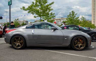 Gümüş renkli Nissan 350Z bronz alaşımlı tekerlekleriyle ikonik tasarımı ve açık hava araba etkinliğinde etkileyici performansı ile tanınıyor.