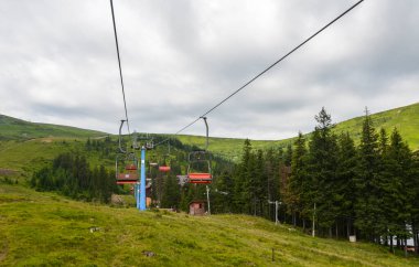 Yeşil tepelerin, sık ormanların ve bulutlu gökyüzünün ortasındaki manzaralı sandalye kaldırışı. Sakin dağ manzarası, açık havada keşif ve rahatlık için ideal sakin bir atmosfer yaratıyor.