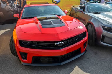 Kırmızı beşinci nesil Chevrolet Camaro. Özel kaput atlatma ve diğer modifikasyonlar onun sportif ve agresif görünümünü geliştirir, kalabalıktan dikkat çekmesini sağlar.