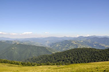 Yeşil ormanlık tepelerin ve açık gökyüzünün altındaki uzak dağların güzel panoramik manzarası. Karpat Dağları, Ukrayna