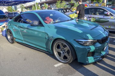 Teal BMW M4 coupe modifiye edilmiş büyük market jantları, ve sportif bir duruş için süspansiyon indirdi, ki bu modern performans estetiğine bir dokunuş ekler