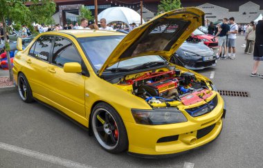 Sarı Mitsubishi Lancer Evolution araba fuarında sergileniyor ve kaput motoru ortaya çıkarmak için açık. Araba modifiye edilmiş, birkaç performans güncellemesi görülebilir.