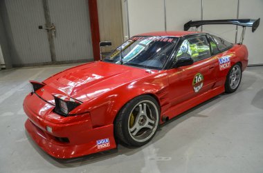 Ağır modifiye edilmiş kırmızı Nissan 200SX S13 geniş arka kanat ve agresif vücut kiti. Araba, performans ve gösteri için üretilen, süspansiyonları indiren pazarlama sonrası tekerleklere sahip.