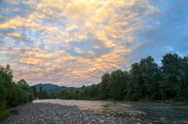 Gün batımında canlı bir gökyüzünün altında, yemyeşil bir nehirden akan Cheremosh Nehri. Doğanın güzelliğini ve dışarıdaki sükuneti göstermek için mükemmel. Karpat Dağları, Ukrayna
