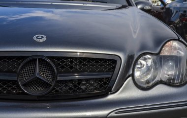 Koyu gri bir Mercedes-Benz 'in detaylı görüntüsü Mercedes yıldızı logosuna odaklanmış. Görüntü arabanın tasarım elementlerini ve markasını vurguluyor