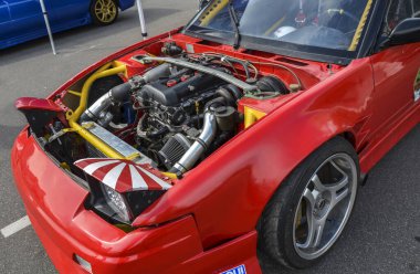 Kırmızı Nissan 200SX S13 kaputu açık, modifiye edilmiş bir motor bölmesi gösteriyor, arabanın özel modifikasyonlarını ve performans odaklarını vurguluyor