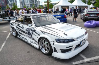 Beyaz Toyota Mark II açık hava etkinliklerinde özel modifikasyonlarla. Arabanın kendine özgü siyah-beyaz grafik tasarımı, pazar sonrası tekerlekleri ve vücut kiti var.