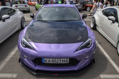 Siyah kapüşonlu ve spor modifikasyonlu göz kamaştırıcı mor Subaru BRZ, canlı bir araba yarışmasında sergileniyor.