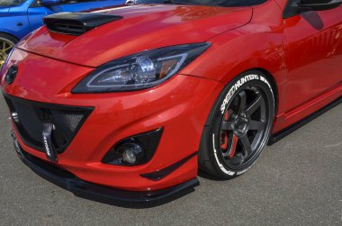 Cesur kırmızı spor MazdaSpeed3 arabası öne çıkan kaput kepçesini, siyah ızgarayı ve özel tekerlekleri sergiliyor. Parlak farları ve çekici kayışı agresif pisti tamamlıyor.