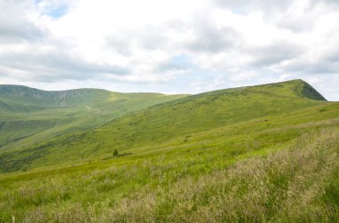 Geniş yeşil tepeler parçalı bulutlu bir gökyüzünün altında sükuneti, huzuru ve doğanın güzelliğini yakalıyor. Karpat Dağları, Ukrayna 