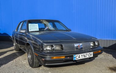 Gri 1985 Oldsmobile Cutlass Ciera, dönemin güvenilir, pratik ve klasik kutu tasarımlarıyla bilinen orta büyüklükte önden çekişli bir arabadır. 