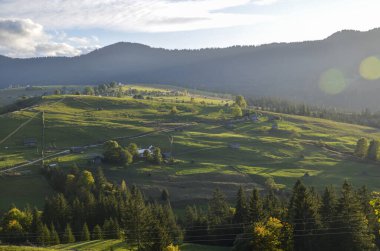 Huzurlu kırsal kesimde yeşil otlaklar, dağınık evler ve yumuşak akşam ışığı altında tepeler sergileniyor. Karpat Dağları, Ukrayna