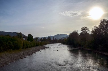 Orman kıyıları arasında yavaşça akan Cheremosh nehrinin sakin manzarası, batan güneşin ılık parıltısı altında, uzak kayan tepelerin arka planıyla. Karpat Dağları, Ukrayna
