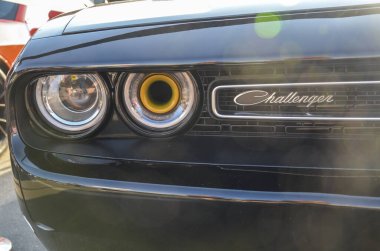 Siyah bir Dodge Challenger 'ın yakın plan fotoğrafı. Benzersiz bir tasarımı var. İçi daire şeklinde bir ışık ve ızgarada Challenger marka bir isim plakası var. 