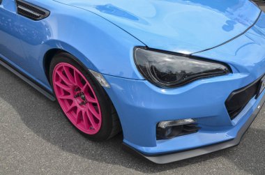 Açık mavi Subaru BRZ 'nin parlak pembe tekerlekleri var. Görüntü arabanın ön tampon farına ve spor tasarımı ve renk kombinasyonunu gösteren tekerleğe odaklanıyor