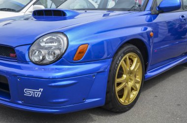 Mavi bir Subaru Impreza WRX STI 'ın ön görüntüsü. Arabada kendine özgü bir kaput kepçesi, altın renkli tekerlekler ve ön tamponda 
