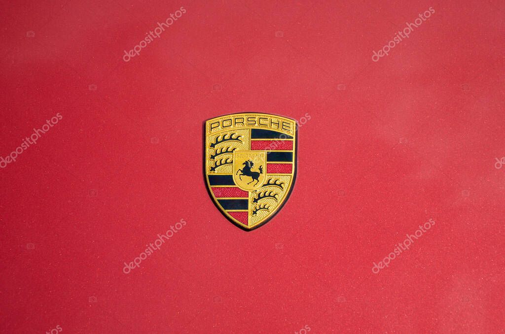 Close-up view of the Porsche emblem against flat, solid red background. The emblem is centered and features the iconic Porsche crest with black horse on a yellow field