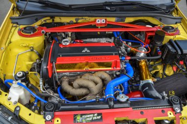 Modifiye edilmiş sarı Mitsubishi Lancer Evrimi motor bölümünün yakın çekimi. Sergide kırmızı bir destek çubuğu, bir 