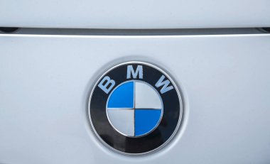 Beyaz bir arabanın üzerindeki BMW logosunun yakın çekimi. Logo, ortasında siyah bir halka ile çevrili 