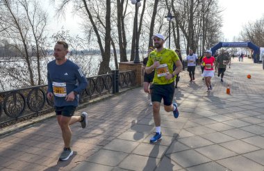 Nehir yolu boyunca koşan bir maratona katılanlar güneşli bir günde açık hava ortamında spor, takım çalışması ve kararlılık gösteriyorlar.