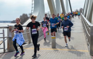 Nehir kenarındaki pitoresk bir köprüde organize bir yarışta aktif olarak koşan çeşitli bireyler.
