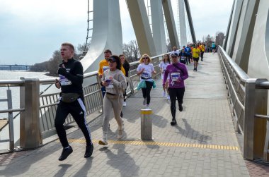 Nehir kenarındaki pitoresk bir köprüde organize bir yarışta aktif olarak koşan çeşitli bireyler.